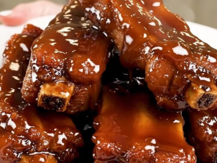 A plate of sticky, glossy glazed pork ribs steaming on a white plate.