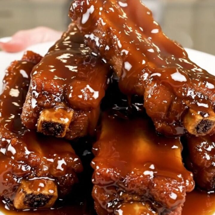 A plate of sticky, glossy glazed pork ribs steaming on a white plate.