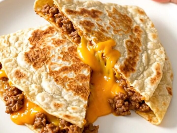 A crispy, golden-brown quesadilla cut into wedges on a white plate, showing a cheesy, beefy filling.