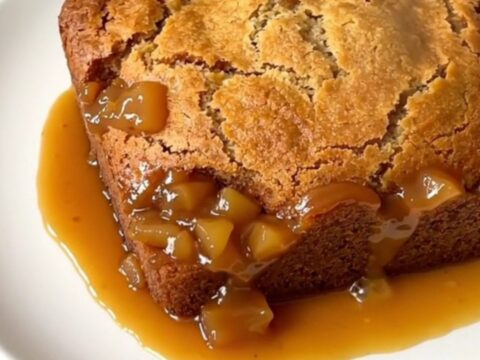 A top-down view of a black slow cooker filled with layers of apple, caramel, and golden cake topping.