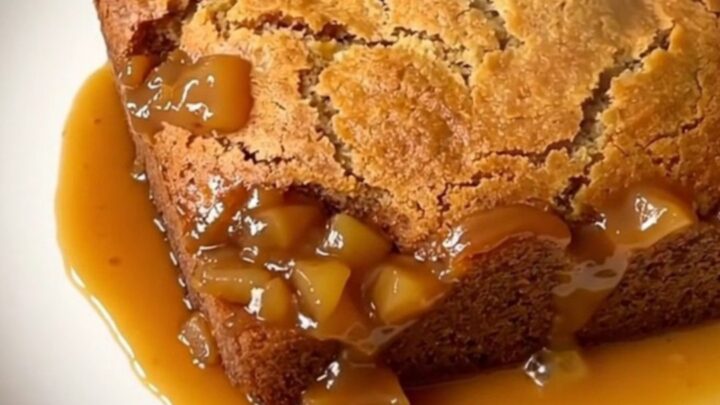 A top-down view of a black slow cooker filled with layers of apple, caramel, and golden cake topping.