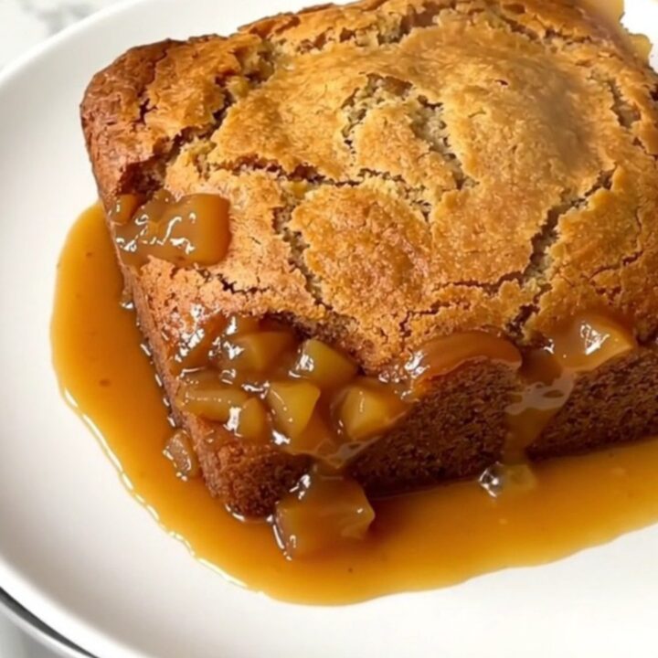 A top-down view of a black slow cooker filled with layers of apple, caramel, and golden cake topping.