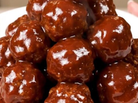 A close-up of glossy barbecue meatballs in a slow cooker, showing the rich, dark sauce and tender texture.