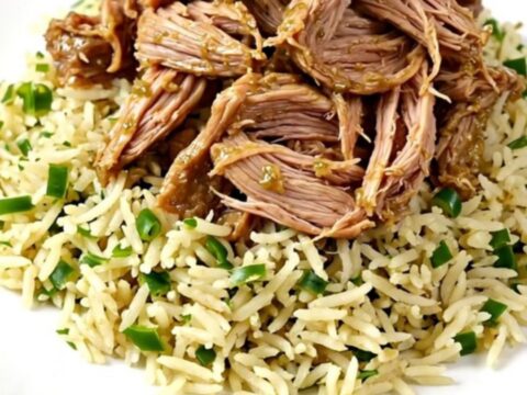 A close-up of tender, shredded salsa verde pork chops served over cilantro lime rice on a white plate.