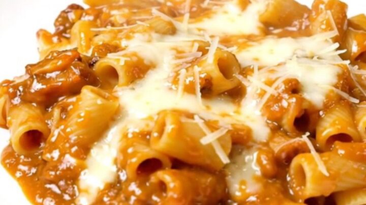 A steaming plate of creamy vodka ziti topped with fresh spinach, captured in a bright kitchen setting.