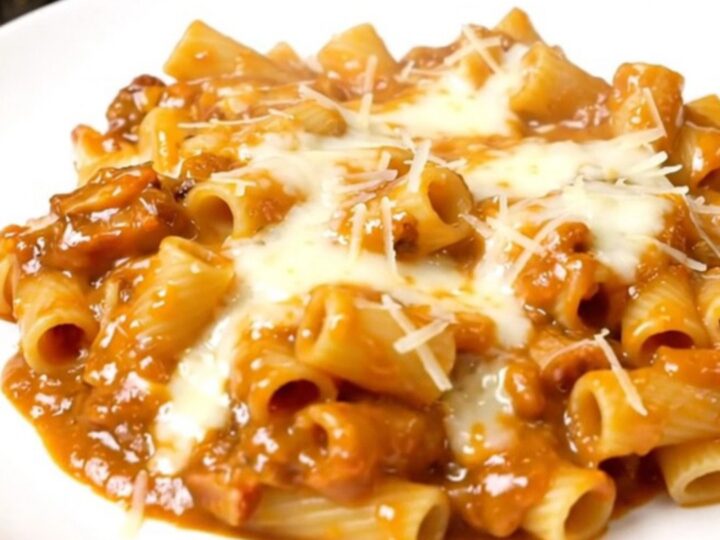 A steaming plate of creamy vodka ziti topped with fresh spinach, captured in a bright kitchen setting.