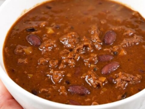 A white bowl filled with rich, glossy beer beef chili, steaming and ready to eat.