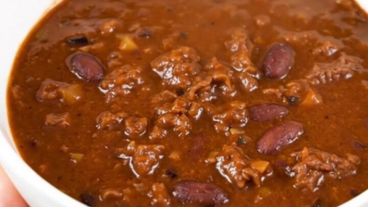 A white bowl filled with rich, glossy beer beef chili, steaming and ready to eat.