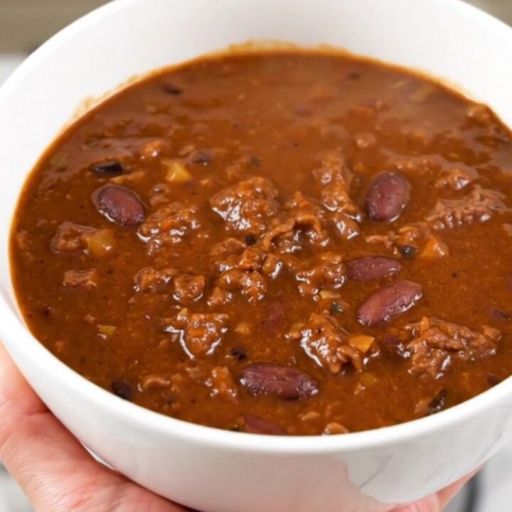 A white bowl filled with rich, glossy beer beef chili, steaming and ready to eat.
