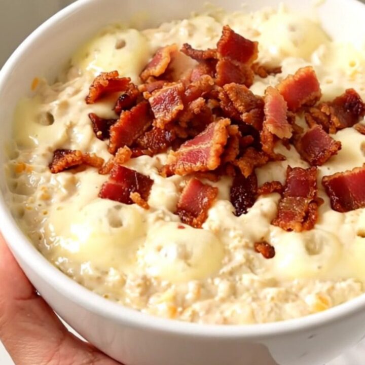 A top-down view of a creamy jalapeno popper dip in a black slow cooker with ingredients arranged on a white countertop.
