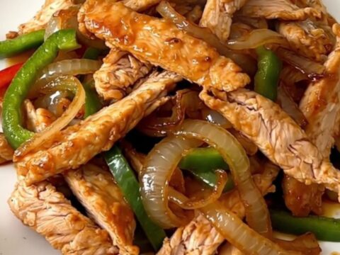 A close-up of sizzling, glossy chicken fajitas with colorful peppers and onions on a white plate.