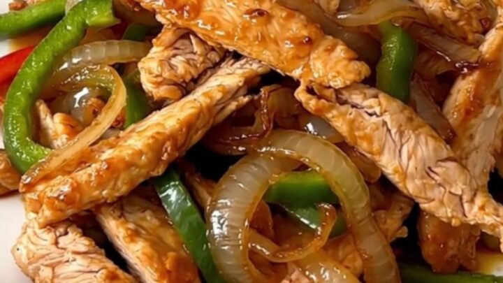 A close-up of sizzling, glossy chicken fajitas with colorful peppers and onions on a white plate.