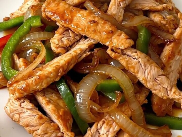A close-up of sizzling, glossy chicken fajitas with colorful peppers and onions on a white plate.