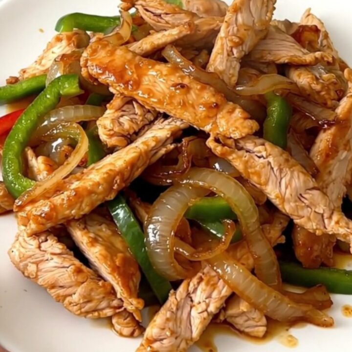 A close-up of sizzling, glossy chicken fajitas with colorful peppers and onions on a white plate.