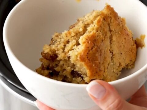 A warm, golden-brown apple butter spice dump cake served in a white bowl with steam rising.