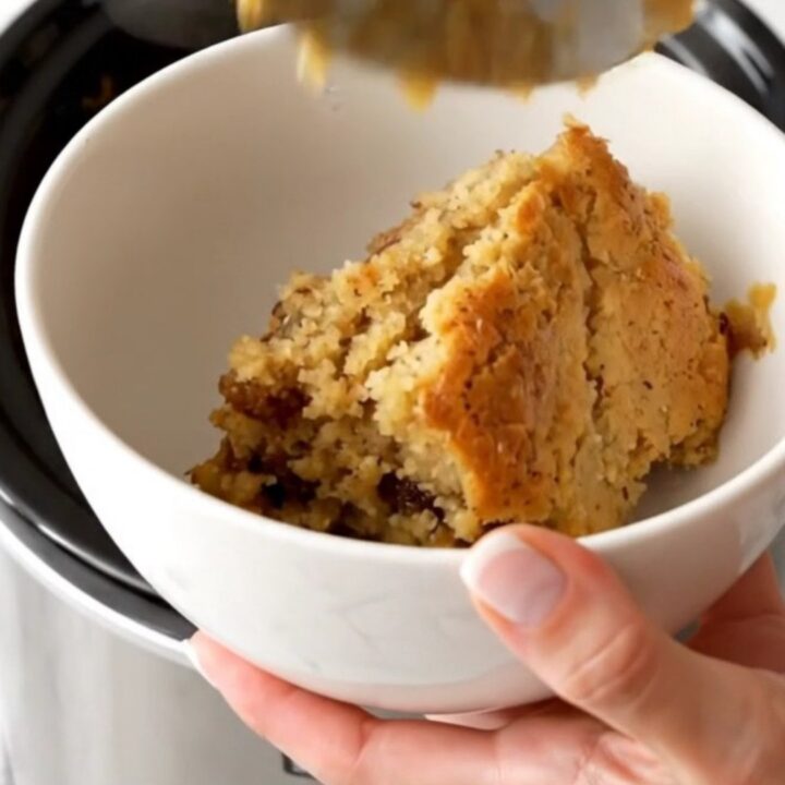 A warm, golden-brown apple butter spice dump cake served in a white bowl with steam rising.