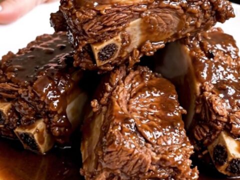 A plate of rich, dark, fall-apart tender braised short ribs served with a glossy pan sauce.