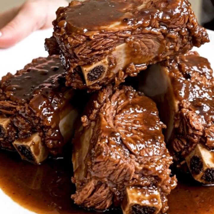 A plate of rich, dark, fall-apart tender braised short ribs served with a glossy pan sauce.