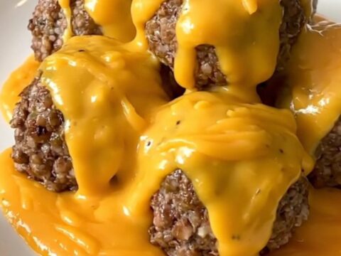 A slow cooker filled with ground beef meatballs covered in a rich cheddar sauce and crumbled bacon.