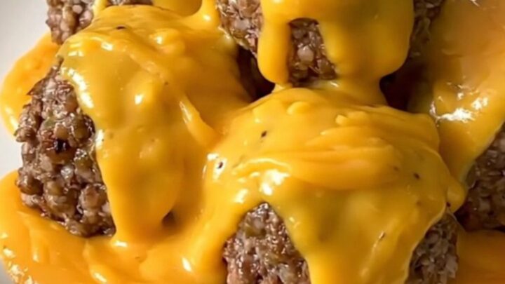 A slow cooker filled with ground beef meatballs covered in a rich cheddar sauce and crumbled bacon.