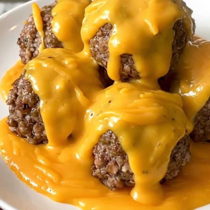 A slow cooker filled with ground beef meatballs covered in a rich cheddar sauce and crumbled bacon.