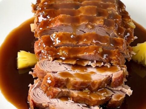 A slow cooker pork roast glazed with pineapple and brown sugar, served on a white plate.