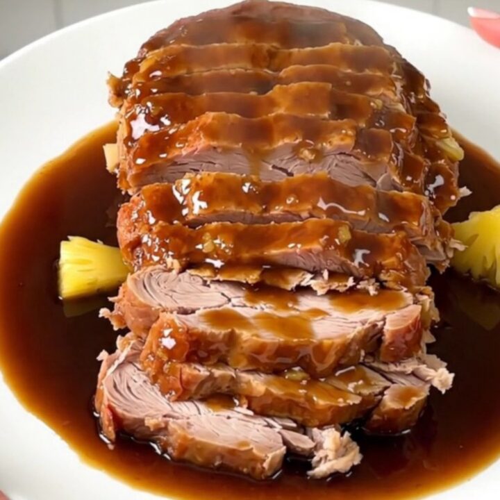A slow cooker pork roast glazed with pineapple and brown sugar, served on a white plate.