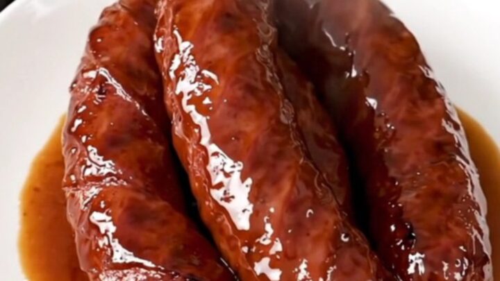 A close-up of glossy, caramelized kielbasa pieces in a rich brown sauce on a white plate.
