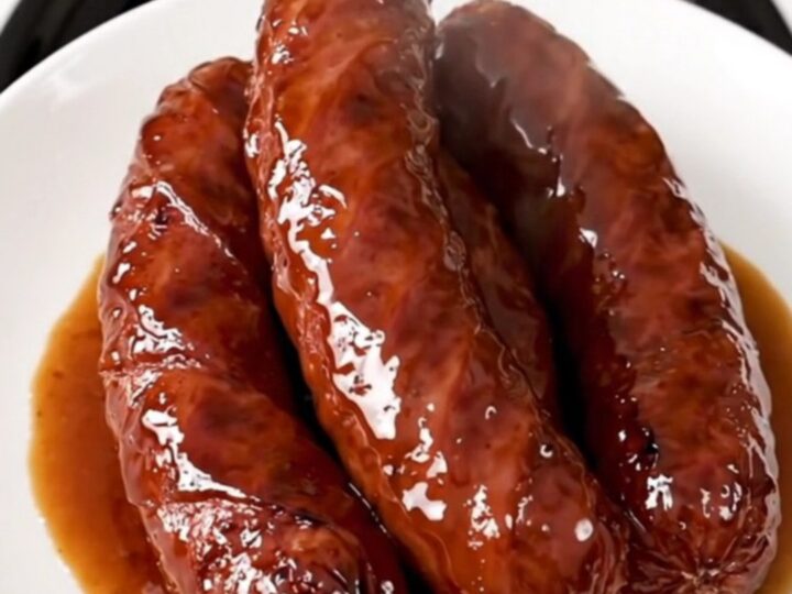 A close-up of glossy, caramelized kielbasa pieces in a rich brown sauce on a white plate.