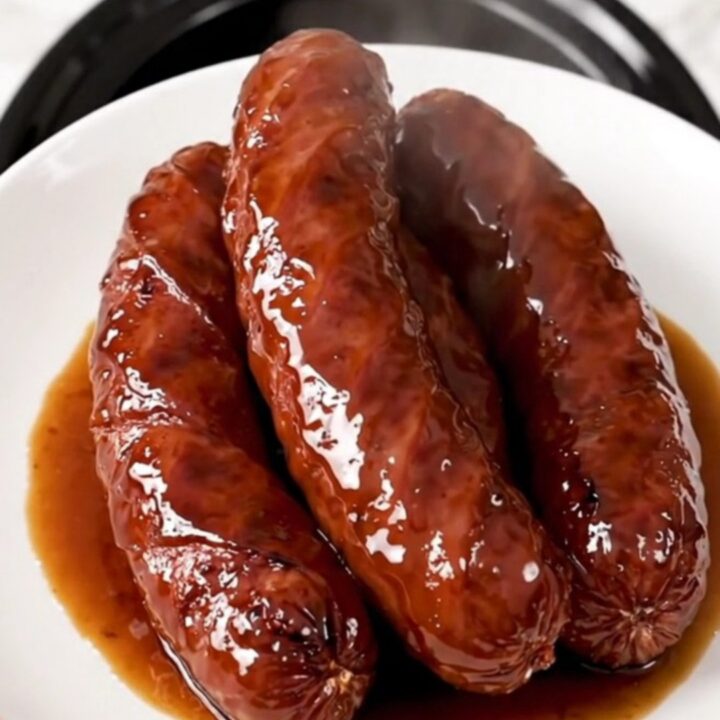 A close-up of glossy, caramelized kielbasa pieces in a rich brown sauce on a white plate.