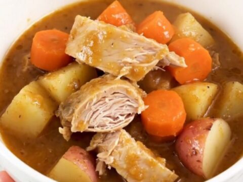 A top-down view of a slow cooker filled with raw turkey, baby carrots, potatoes, and apple cider.