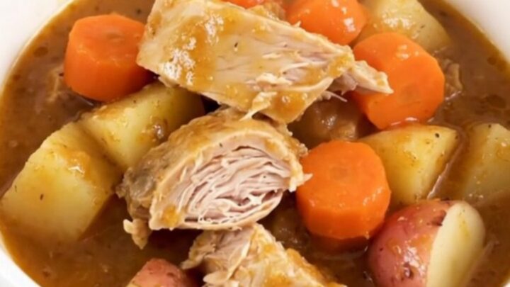 A top-down view of a slow cooker filled with raw turkey, baby carrots, potatoes, and apple cider.