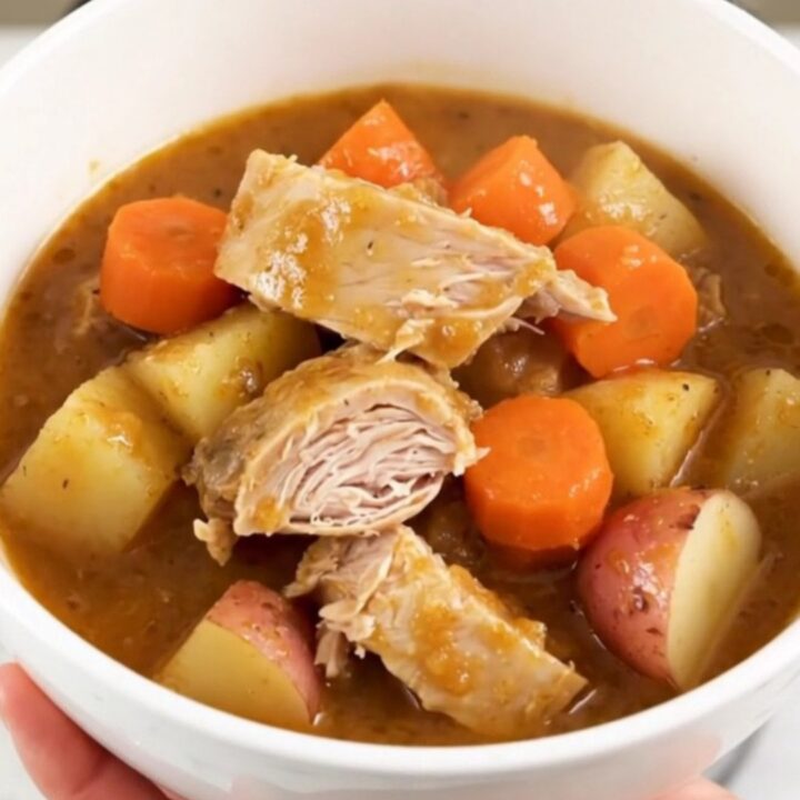 A top-down view of a slow cooker filled with raw turkey, baby carrots, potatoes, and apple cider.
