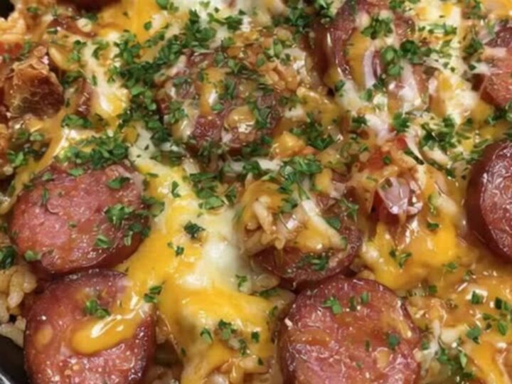 A bubbling cast iron skillet filled with seasoned rice, seared smoked sausage, and melted cheddar cheese.