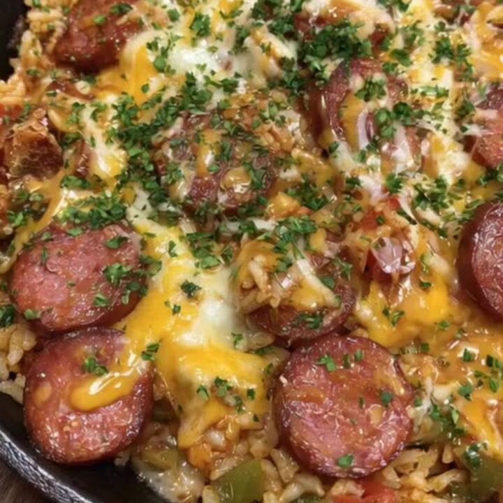 A bubbling cast iron skillet filled with seasoned rice, seared smoked sausage, and melted cheddar cheese.