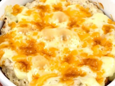 A creamy, melted loaded baked potato dip in a black slow cooker, topped with fresh green onions and cheddar.