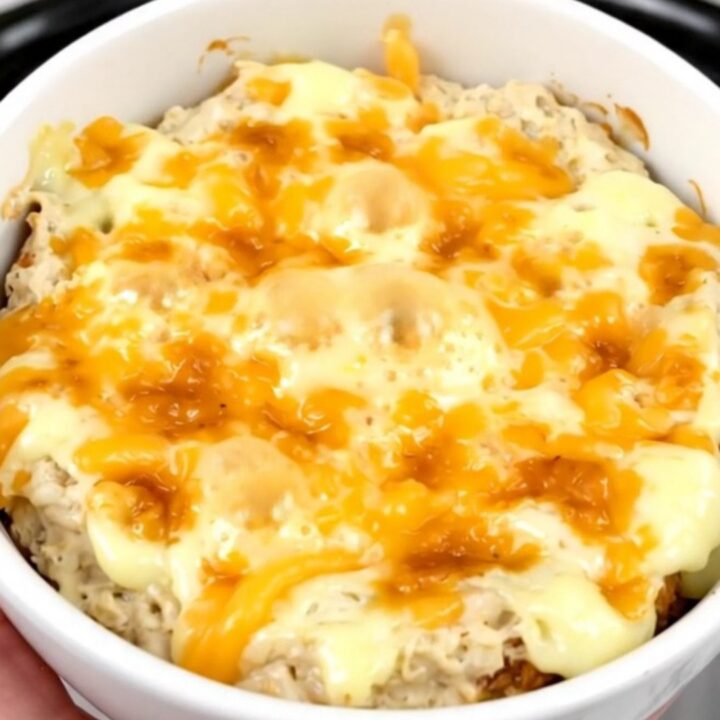 A creamy, melted loaded baked potato dip in a black slow cooker, topped with fresh green onions and cheddar.