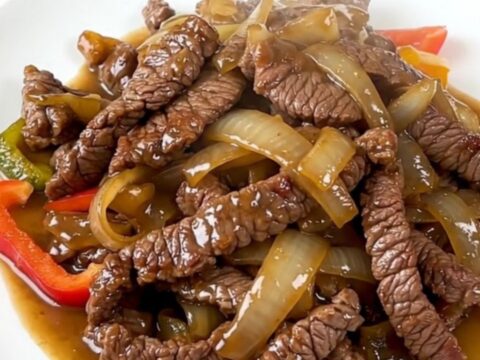 A plate of tender, slow-cooked flank steak fajitas with colorful bell peppers and onions.