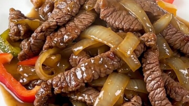 A plate of tender, slow-cooked flank steak fajitas with colorful bell peppers and onions.