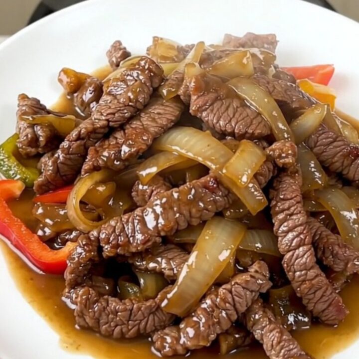 A plate of tender, slow-cooked flank steak fajitas with colorful bell peppers and onions.