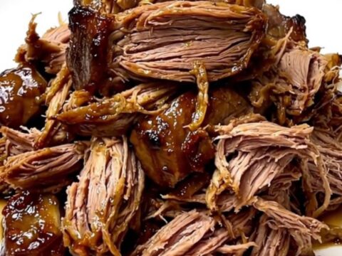 A slow cooker filled with a tender beef chuck roast seasoned with dill pickles and ranch spices on a white countertop.