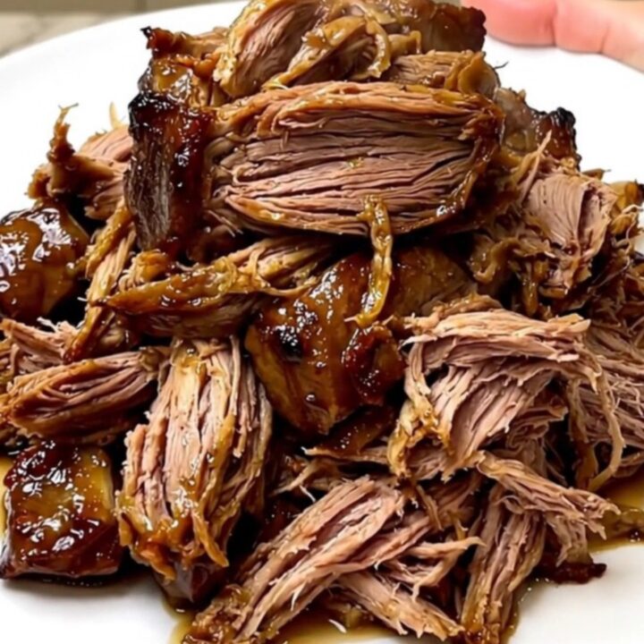 A slow cooker filled with a tender beef chuck roast seasoned with dill pickles and ranch spices on a white countertop.