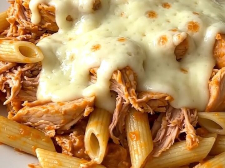 A close-up of creamy shredded chicken with roasted red peppers served over penne pasta in a white bowl.