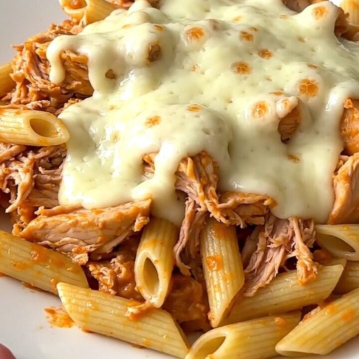 A close-up of creamy shredded chicken with roasted red peppers served over penne pasta in a white bowl.