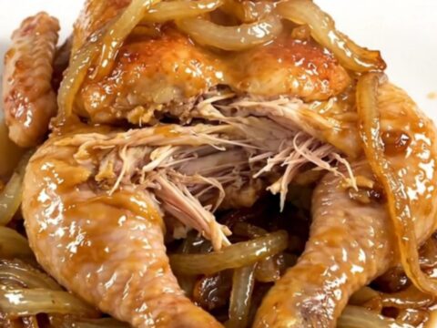 A whole cooked chicken inside a slow cooker surrounded by tender onions and savory broth.