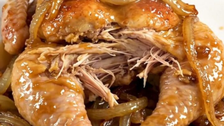A whole cooked chicken inside a slow cooker surrounded by tender onions and savory broth.