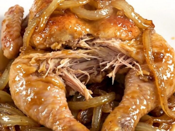A whole cooked chicken inside a slow cooker surrounded by tender onions and savory broth.