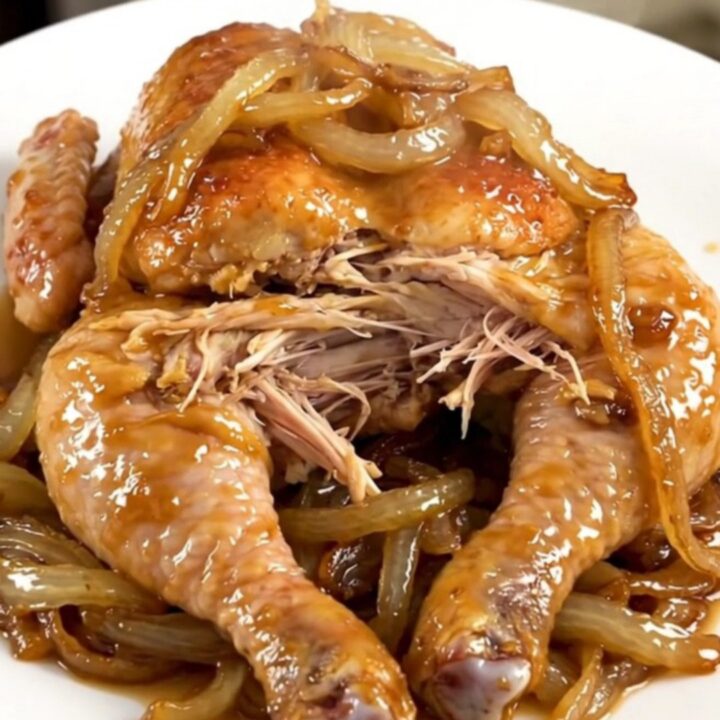 A whole cooked chicken inside a slow cooker surrounded by tender onions and savory broth.