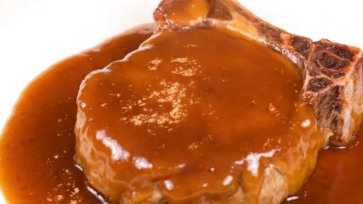 A close-up of a glazed peach BBQ pork chop on a white plate with visible steam.
