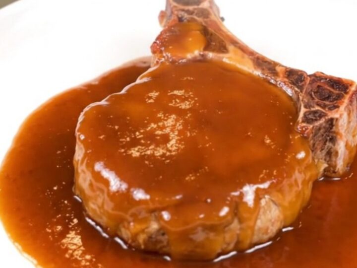 A close-up of a glazed peach BBQ pork chop on a white plate with visible steam.